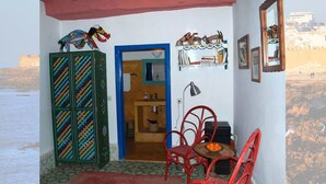 A room with a view of the sea, a colorful cabinet, a red chair, a small table with oranges, and a shelf with decorative items. - Riad Dar Latifa (Essaouira)