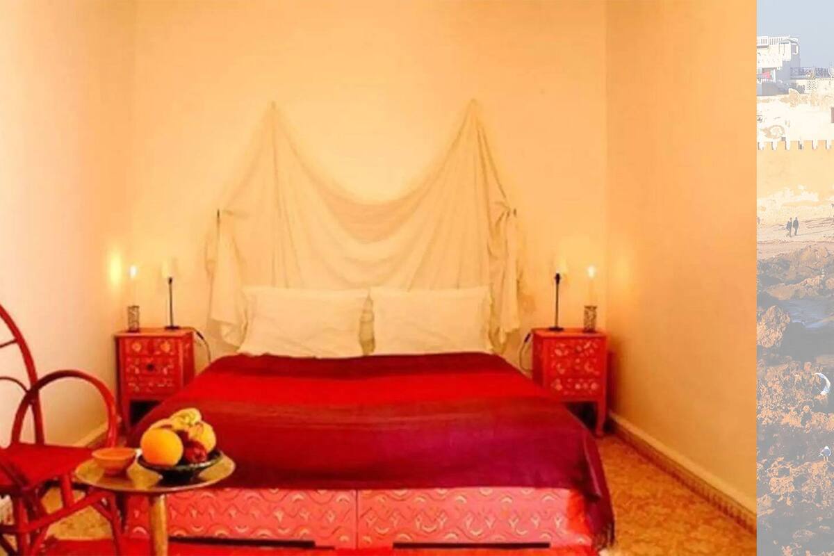 A bedroom with a bed, a nightstand, a chair, and a table with fruit.