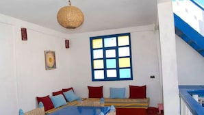 A room with a large blue table, a woven ceiling light, a colorful window, and a patterned rug. - Riad Dar Latifa (Essaouira)