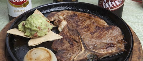 Un plato con un bistec, cebolla y guacamole.