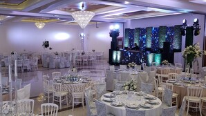 A banquet hall with round tables set for dining, a stage with a DJ booth, and decorative lighting. - Hotel Paradise Inn (Ciudad Victoria)