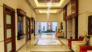 A hotel lobby with a marble floor, red and cream-colored sofas, a chandelier, and a view of a garden through the glass doors. - Hotel Paradise Inn (Ciudad Victoria)