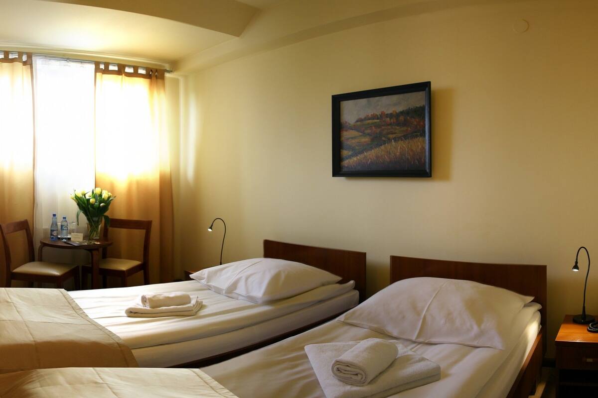 Een hotelkamer met twee eenpersoonsbedden, een bureau, een stoel, een televisie en een schilderij aan de muur.
