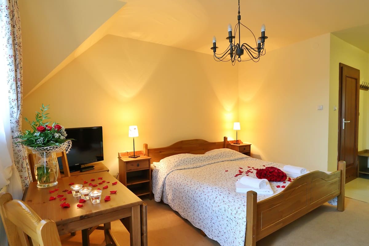 Een knus slaapkamer met een houten bed, een televisie, een bureau met lamp en een kroonluchter.