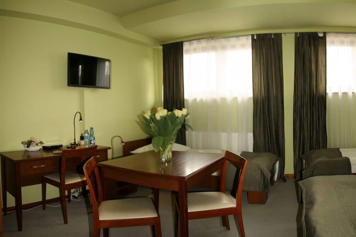 Een hotelkamer met twee bedden, een bureau met stoel, een aan de muur bevestigde televisie en een raam met gordijnen.