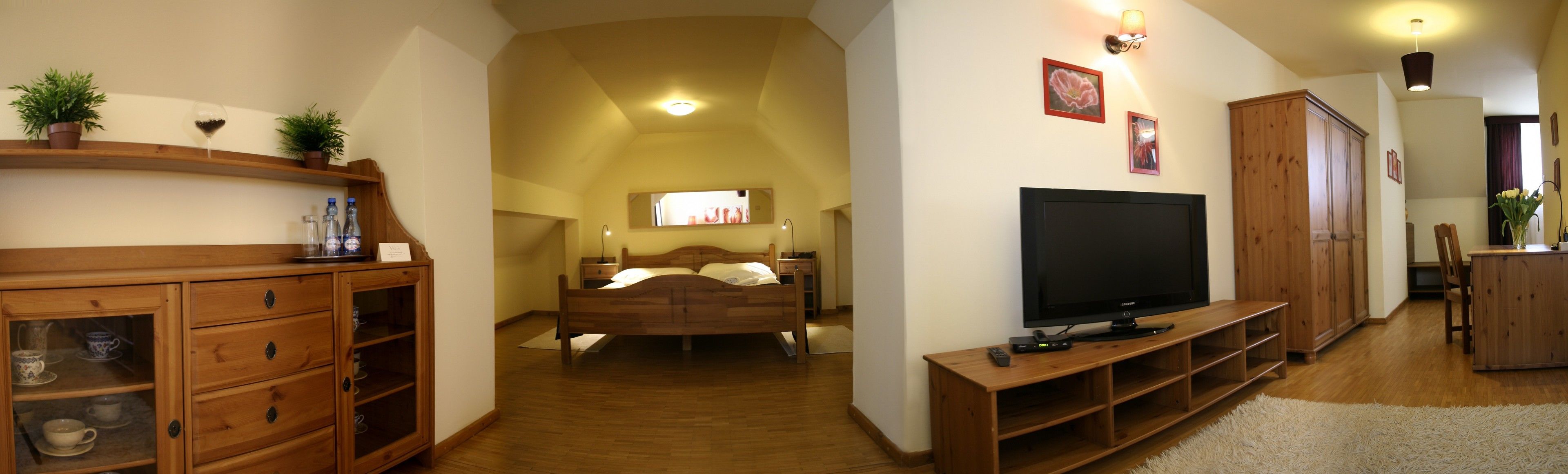A spacious bedroom with a large bed, a TV, wooden furniture, and a small bathroom visible through an archway.