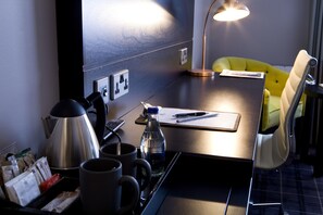 Habitación de hotel con escritorio, una silla amarilla, cafetera, botella de agua y lámpara.