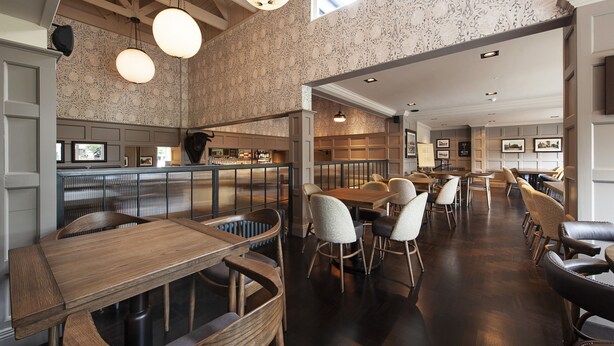 Ein Restaurant mit Holztischen und -stühlen, einer Bar und einem Innenraum mit gemustertem Wandpapier.
