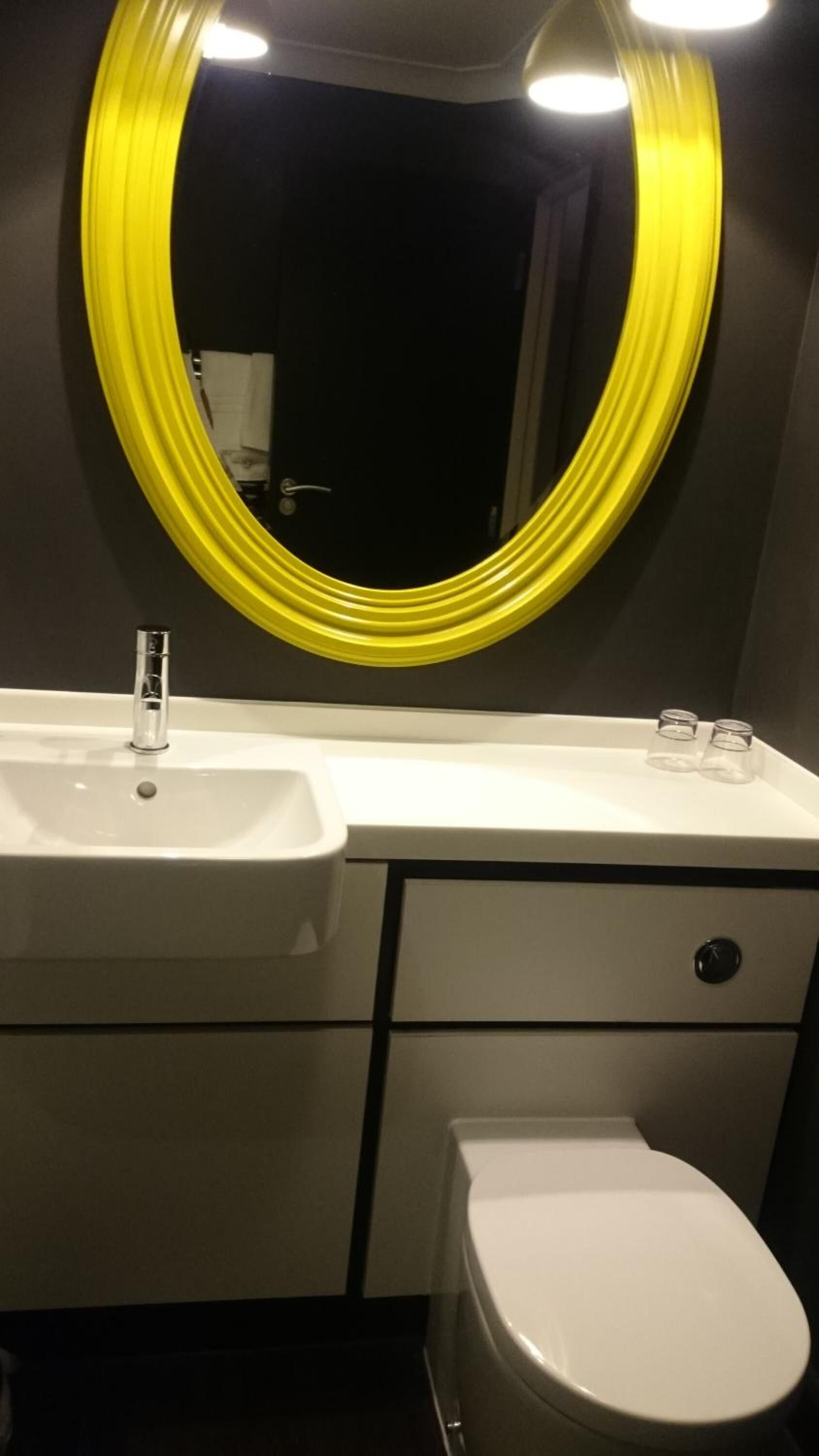 Ein Badezimmer mit einem weißen Waschbecken, einem Spiegel mit gelbem Rahmen und einer Toilette.