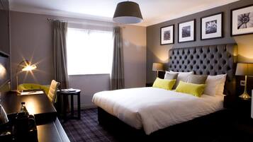 A hotel room with a large bed, a desk, a chair, a lamp, and a window with curtains.