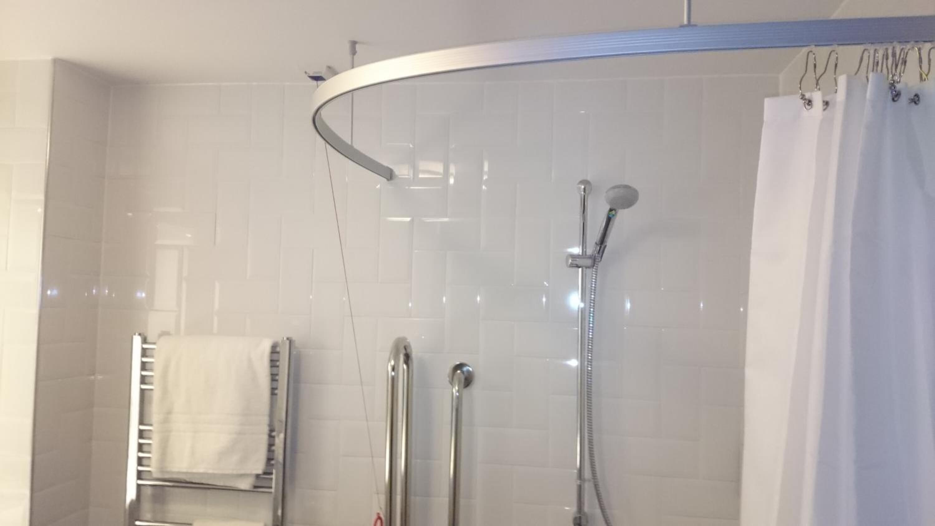 Et moderne badeværelse med en brusekabine i glas, et håndklædetørrestativ og et brusehoved.
