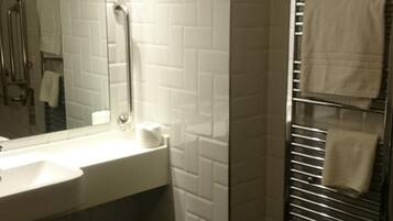 A modern bathroom with a large mirror, white tiles, a sink, and a towel rack.