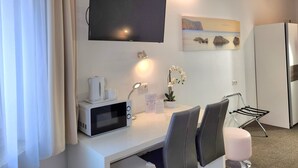A modern hotel room with a flat-screen TV, a microwave, a small table with a coffee maker, a potted plant, and a seating area with chairs and a cushioned stool. - Hotel Michael (Gerasdorf bei Wien)