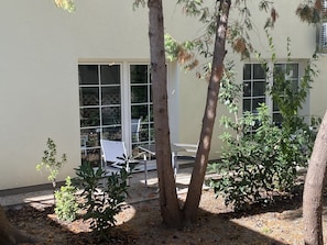 Un patio con mesa y sillas, rodeado de árboles y un edificio con grandes ventanales.