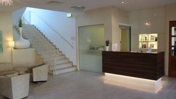 A modern hotel lobby with a reception desk, a staircase, and seating areas.