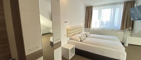 A hotel room with a large mirror, a bed with two pillows, a small bedside table, and a radiator.