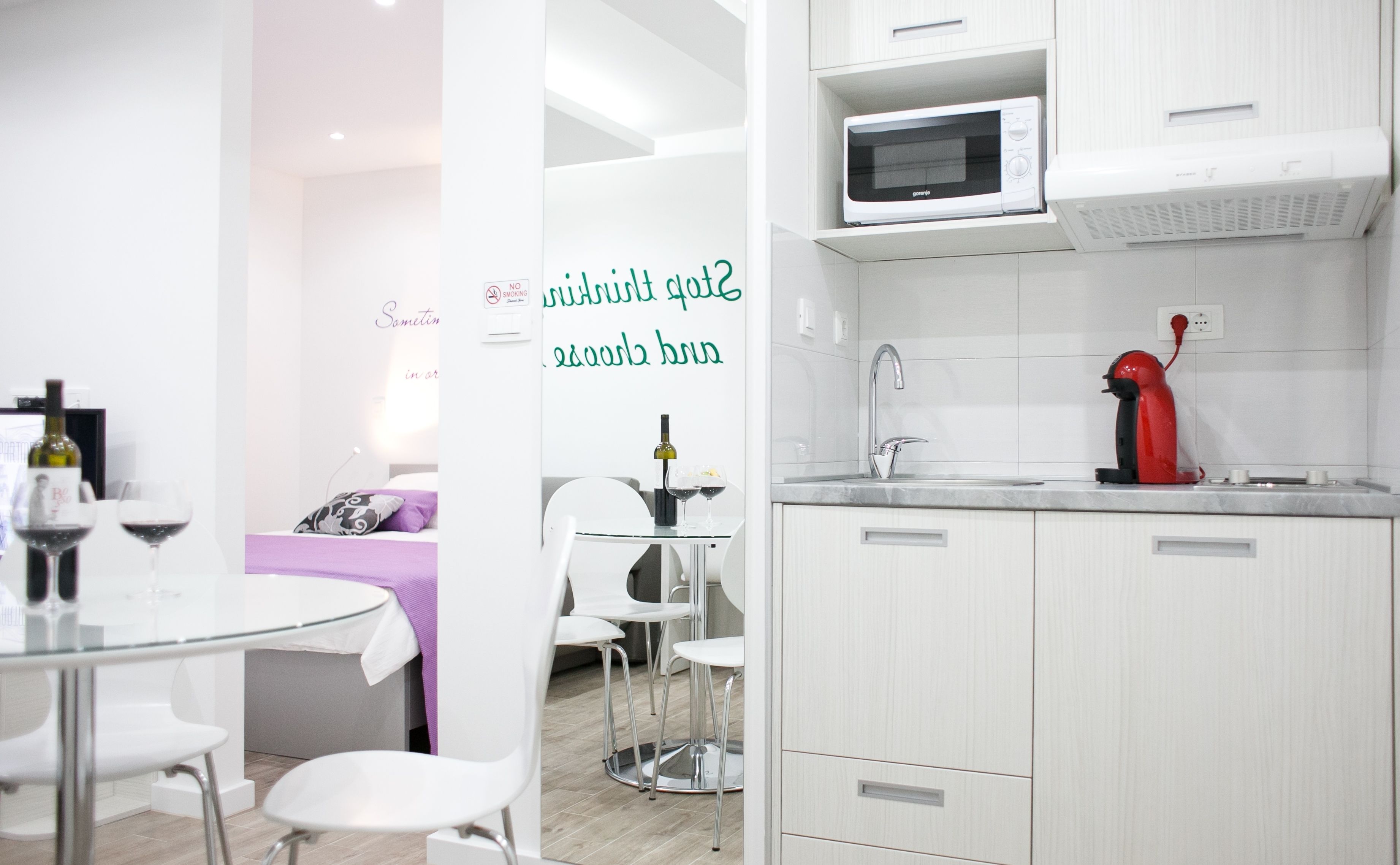A modern kitchen with white cabinets, a microwave, a red kettle, and a sink.