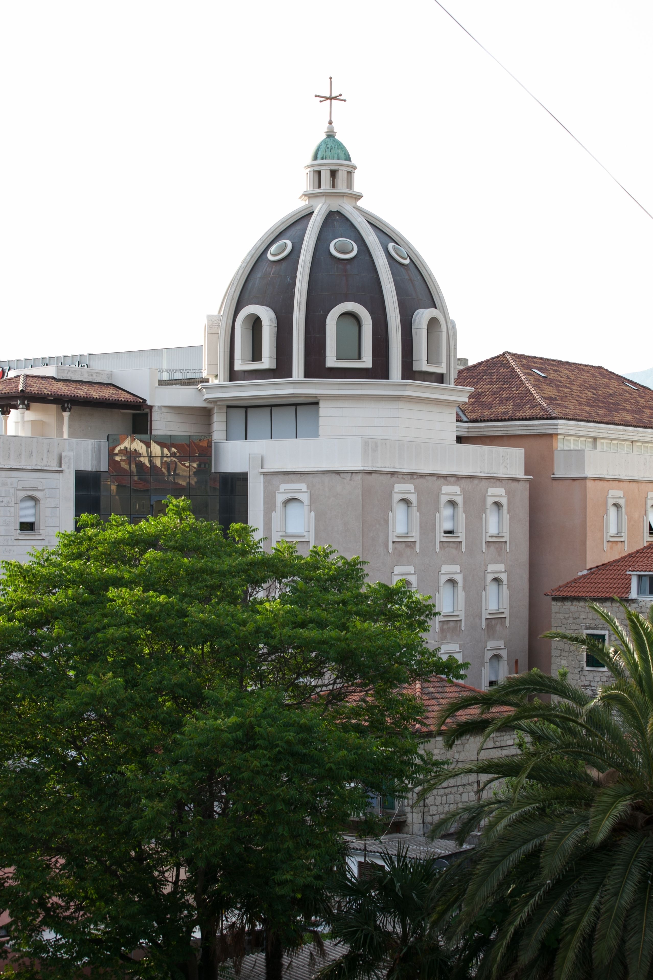 A building with a prominent dome and a cross on top, surrounded by other buildings and trees.