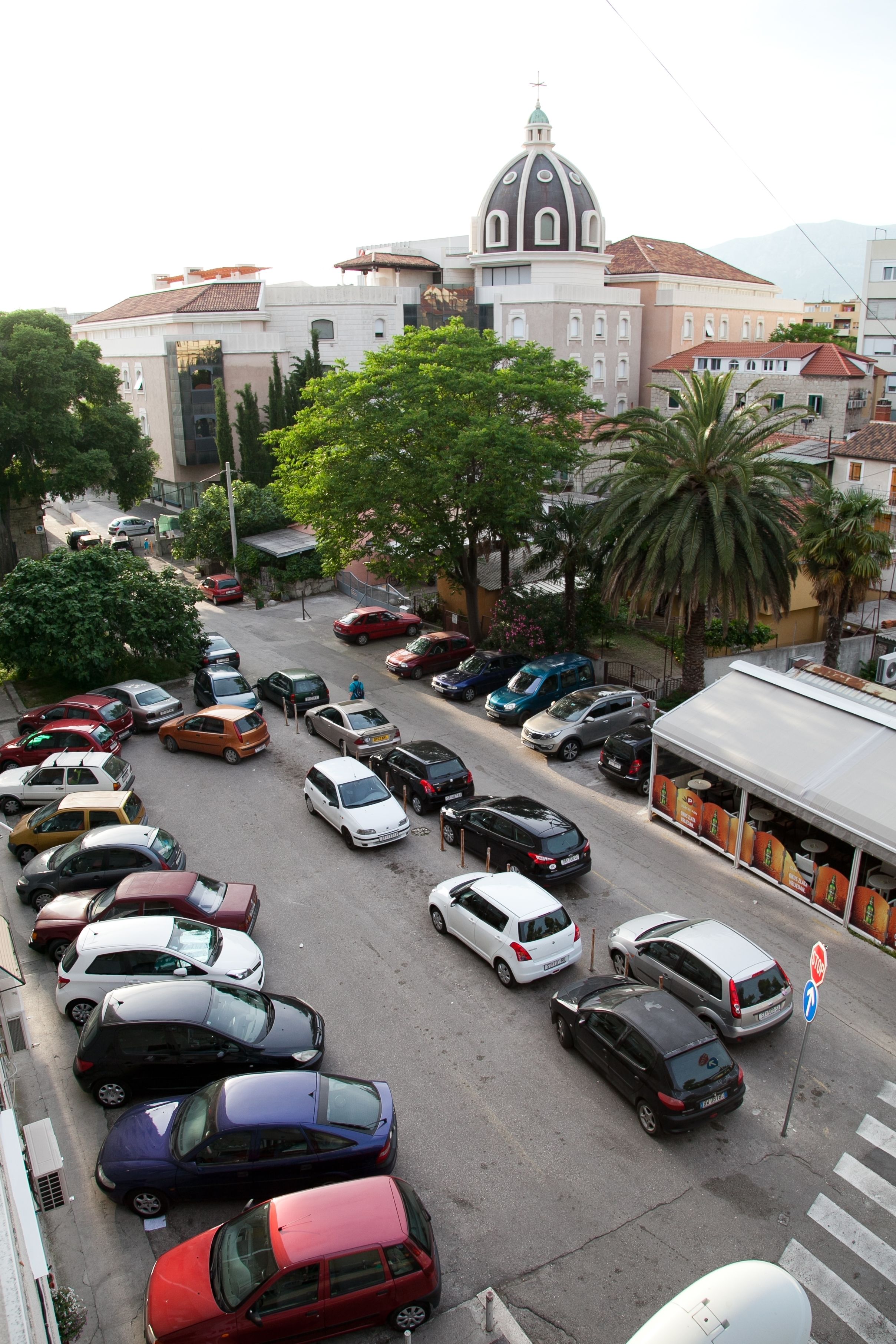 Un parking où sont garées différentes voitures, avec un bâtiment surmonté d’un dôme en arrière-plan.