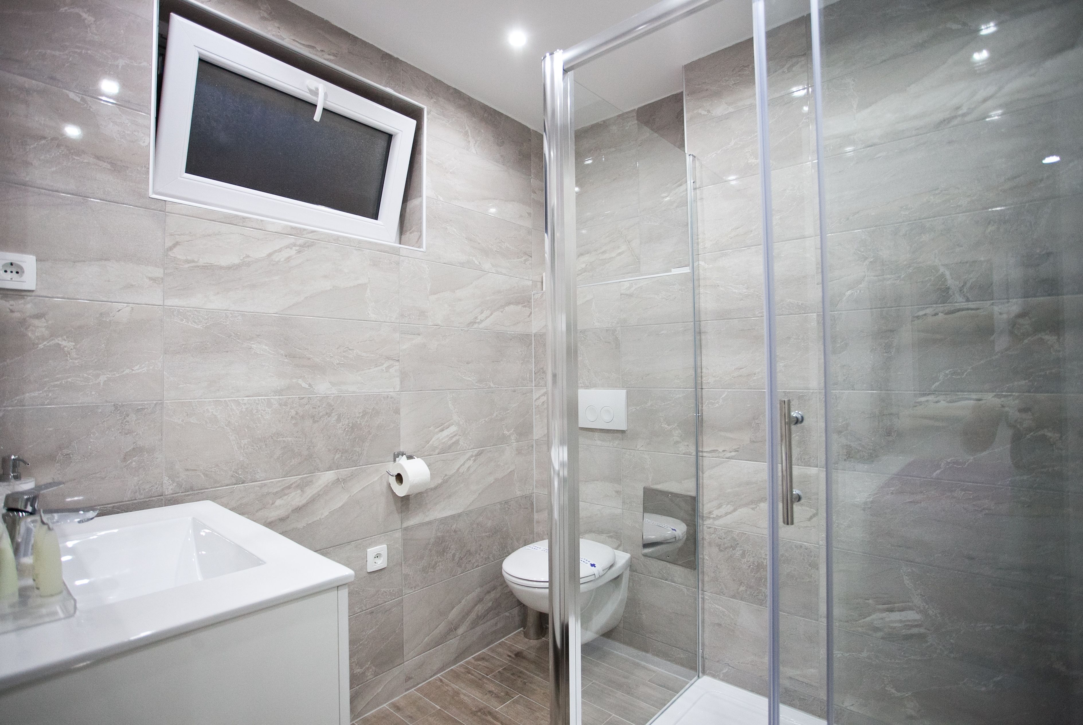 Un baño moderno con cabina de ducha de vidrio, un lavabo blanco y un inodoro.