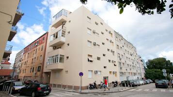 Un immeuble à plusieurs étages doté de balcons, avec des voitures garées et un passage piéton.