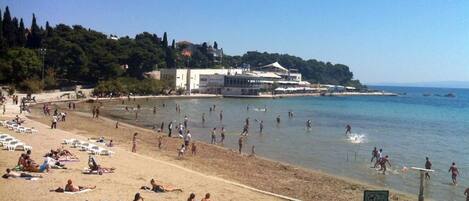 A beach with sunbathers, a clear sky, and a building with a sign that reads "MEDICINA".