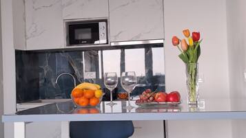 A modern kitchen with a marble backsplash, a built-in microwave, and a glass island with fruit and wine glasses.