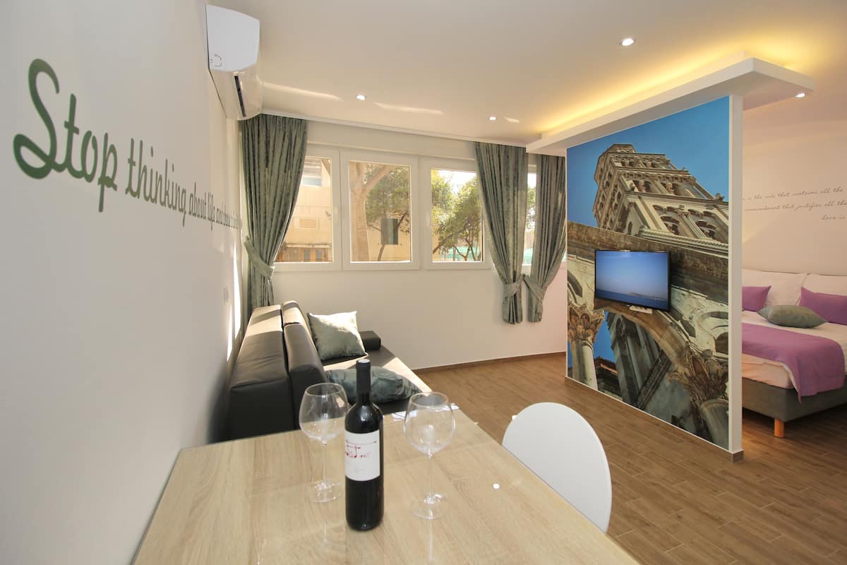 Une chambre d’hôtel comprenant un coin repas, un canapé, une télévision et une fresque murale représentant un bâtiment.