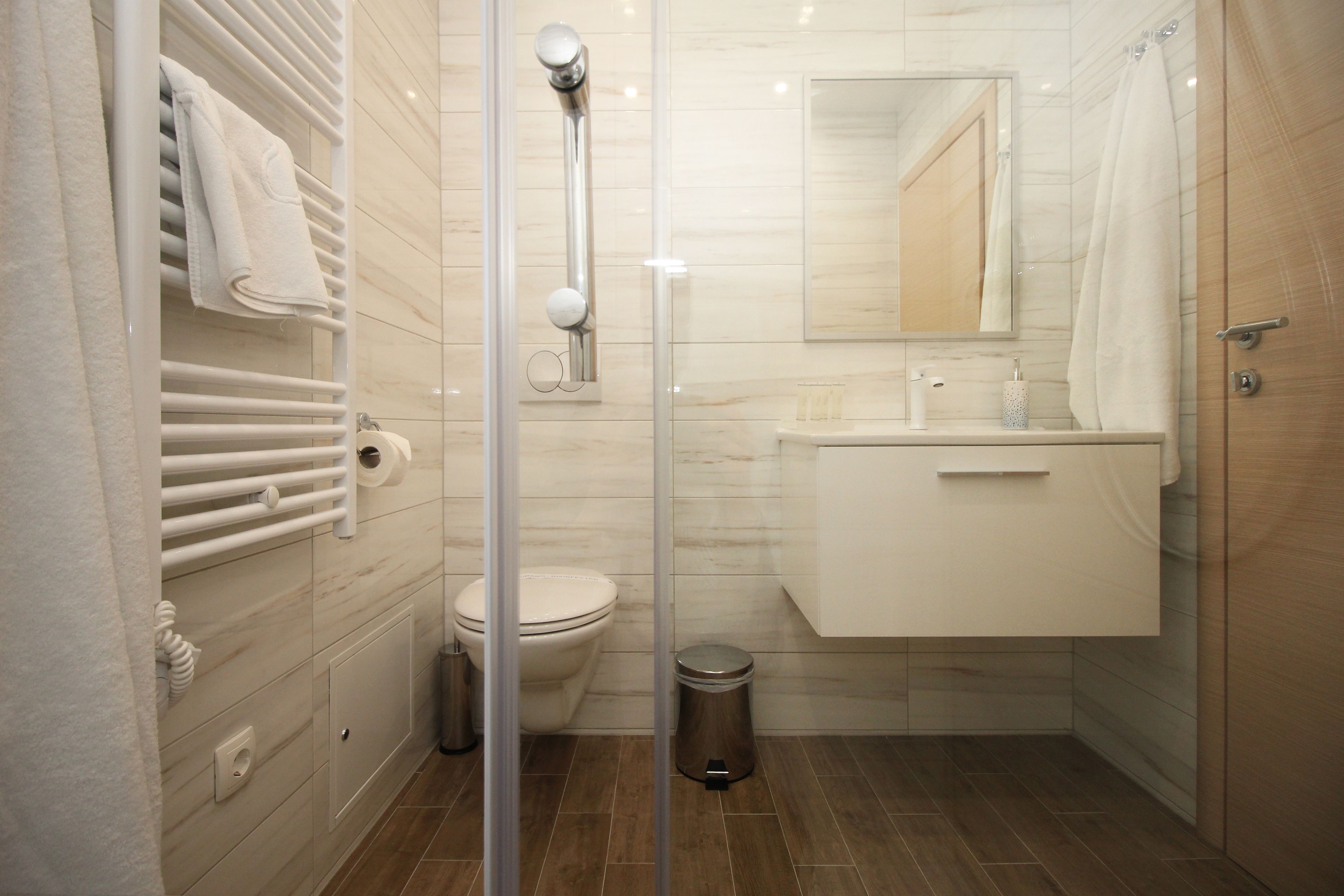 A modern bathroom with a glass shower enclosure, a toilet, a sink with a mirror, and a towel rack.
