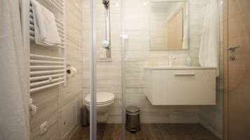 A modern bathroom with a glass shower enclosure, a toilet, a sink with a mirror, and a towel rack.