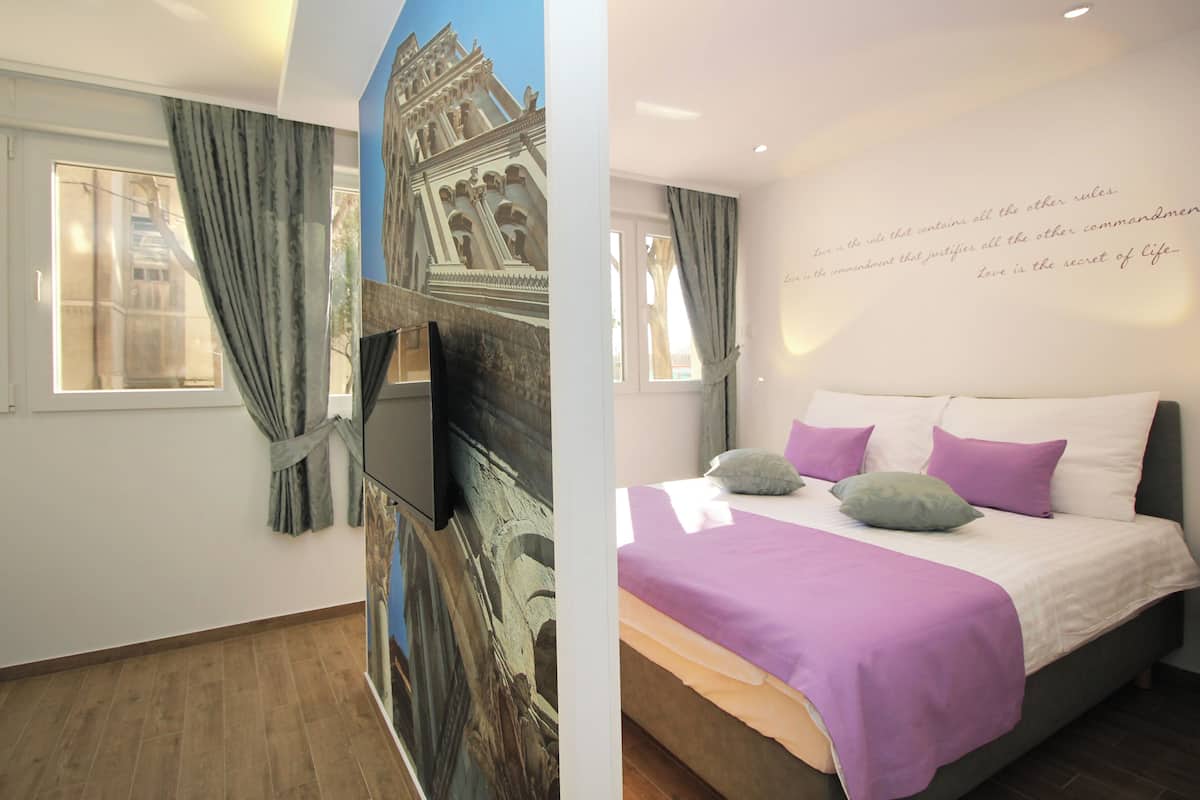 Une chambre à coucher avec un lit, des oreillers, une télévision et une fresque représentant un bâtiment.