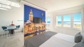 A hotel room with a bed, a desk with chairs, a large window with a view of the sea, and a mural of a cityscape. - Apartments 4 You in Split (Split)