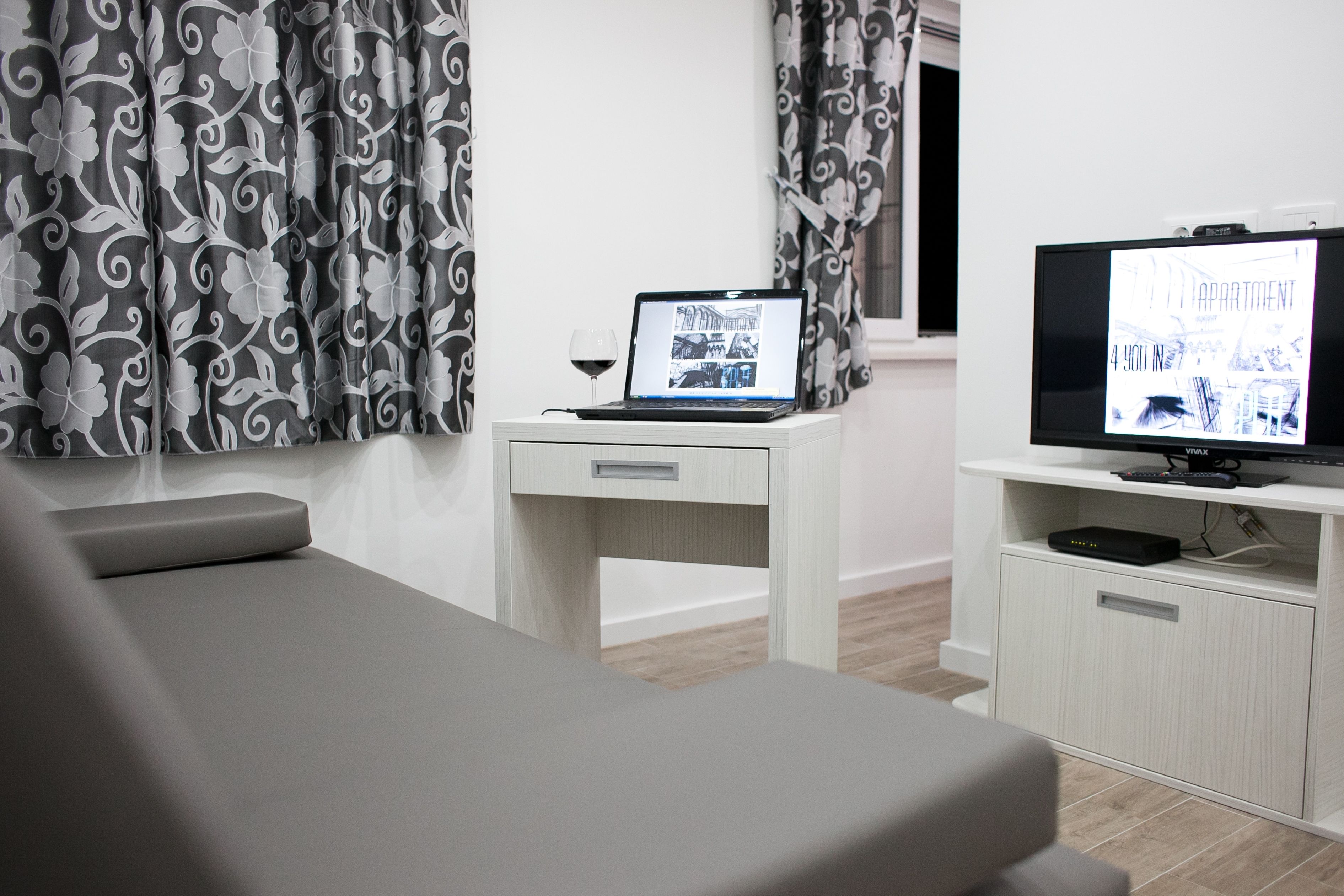 Une chambre d’hôtel moderne équipée d’un lit, d’un bureau avec un ordinateur portable, d’une télévision et de rideaux à motifs.