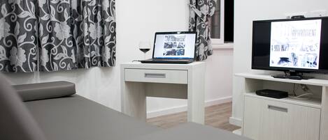 Une chambre d’hôtel moderne équipée d’un lit, d’un bureau avec un ordinateur portable, d’une télévision et de rideaux à motifs.