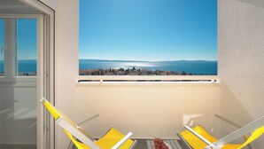 A balcony with two yellow chairs and a table, overlooking a coastal view with a clear sky. - Apartments 4 You in Split (Split)