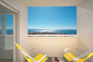 Ein Balkon mit zwei gelben Stühlen und einem Tisch, der Blick auf die Küste und einen klaren Himmel bietet.