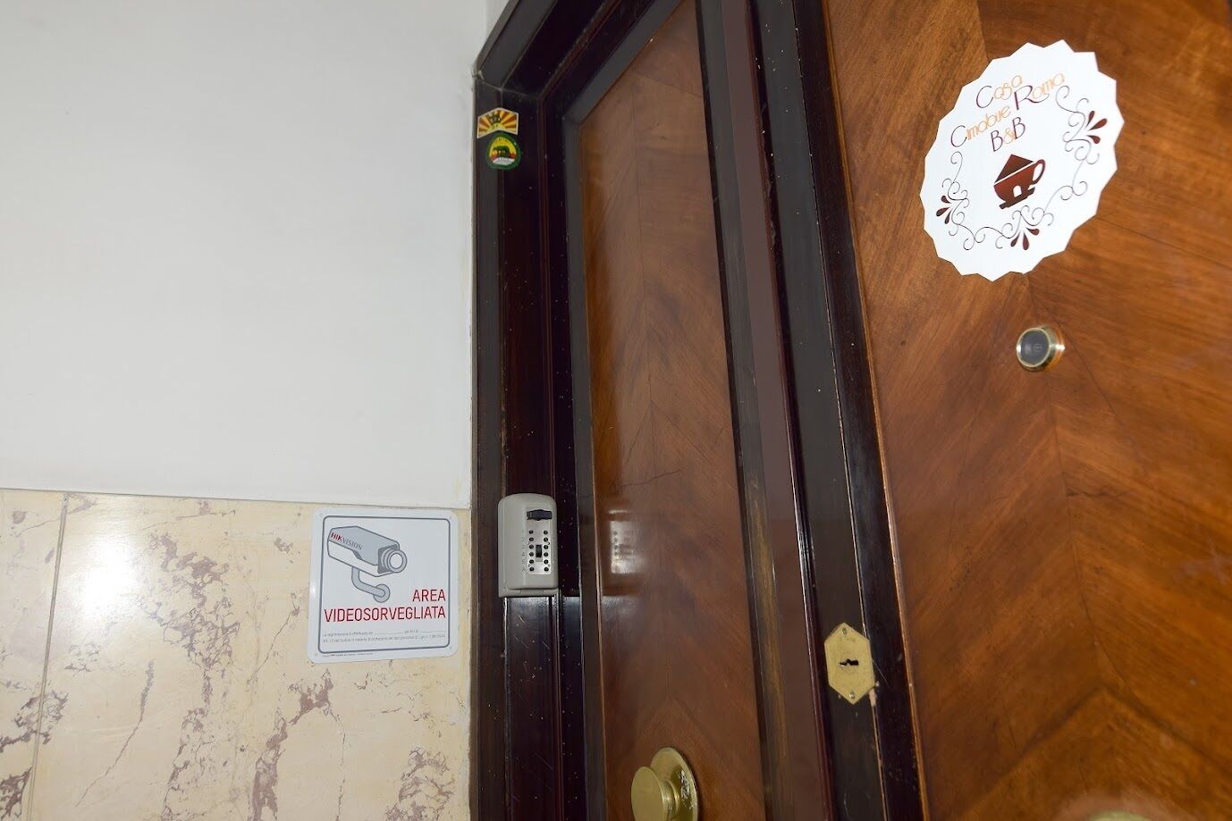 Een houten deur met een beveiligingscodeklavier en een sticker met een afbeelding van een huis en een kopje.