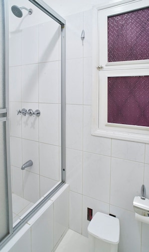 Een badkamer met een douchecabine, een toilet en een raam met paars getinte glas.