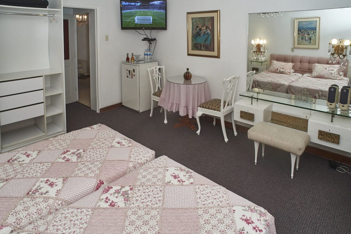 Ein Schlafzimmer mit einem großen Bett, einem Schminktisch, einem Frisierkasten, einem Sessel, einem kleinen Tisch und einem Fernseher.