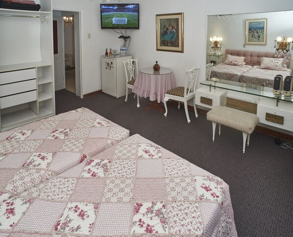 A bedroom with a large bed, a dresser, a vanity, a chair, a small table, and a television. - B&B El Olivar (Lima)