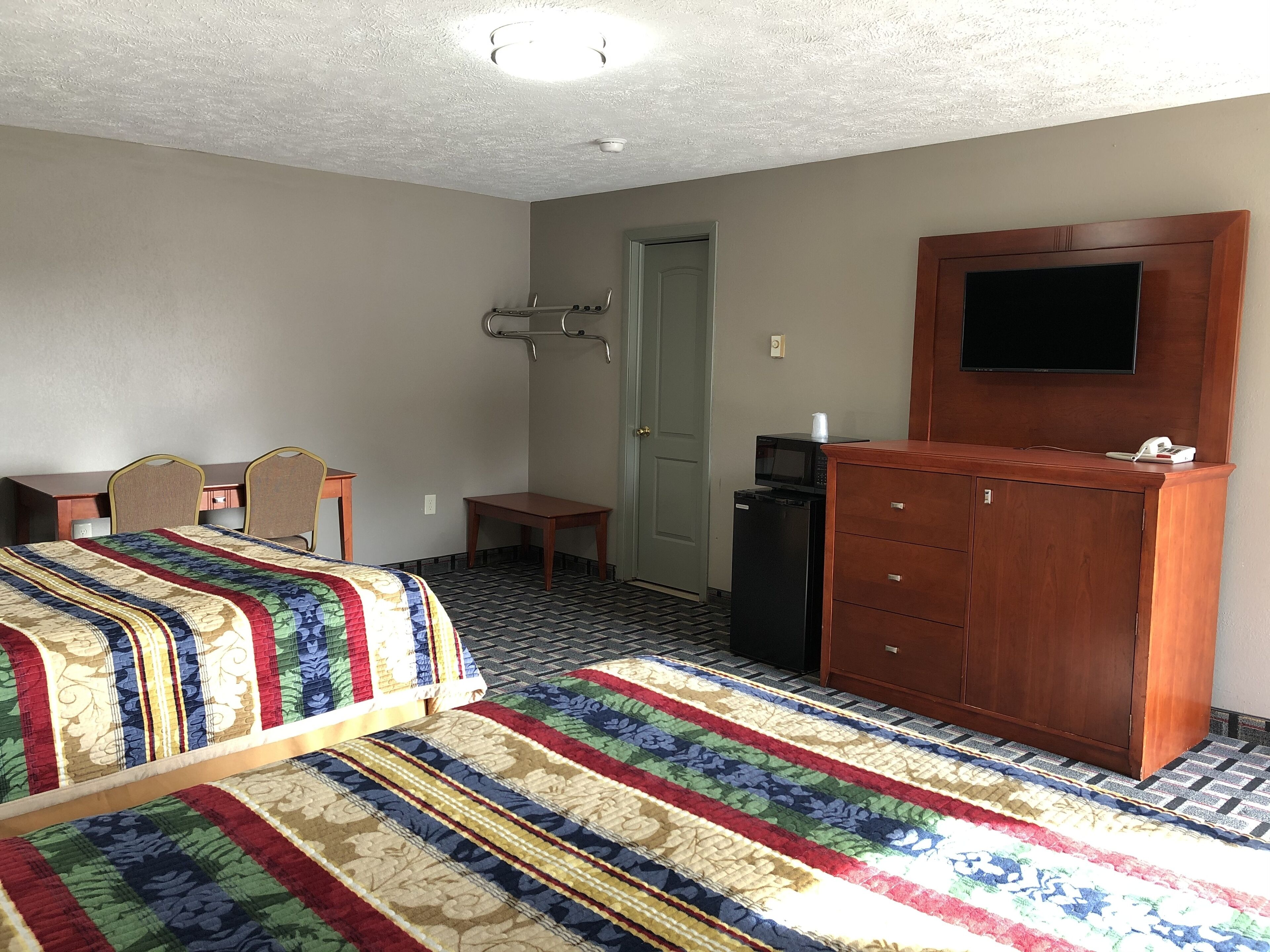 A hotel room with two beds, a desk, a chair, a television, a microwave, and a small refrigerator.