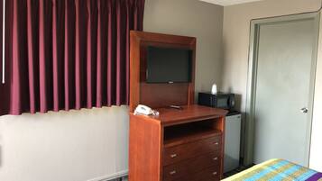 A hotel room with a wooden desk, a television, a telephone, a microwave, and a bed with a striped bedspread.