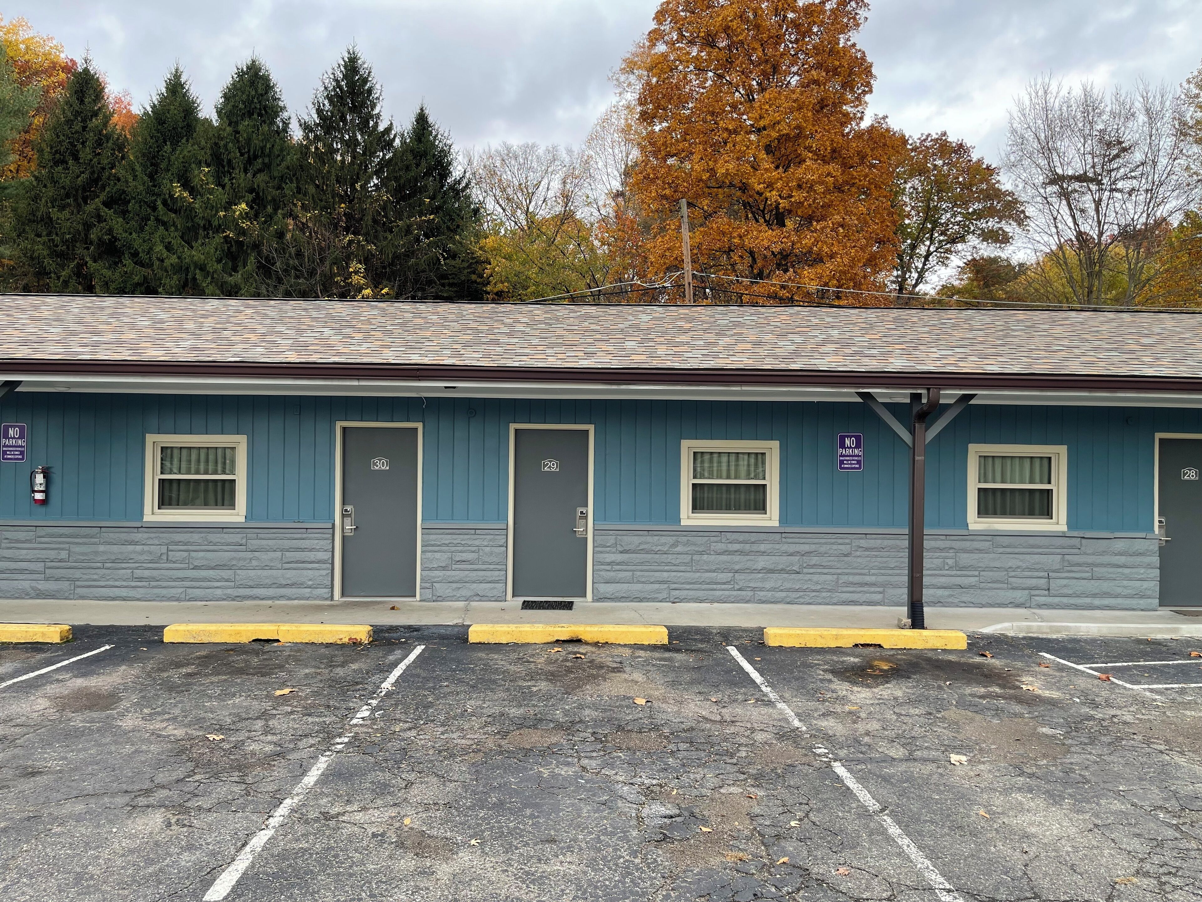 Un motel con puertas numeradas, un estacionamiento y una fila de árboles con follaje otoñal.
