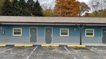 Un motel con puertas numeradas, un estacionamiento y una fila de árboles con follaje otoñal.