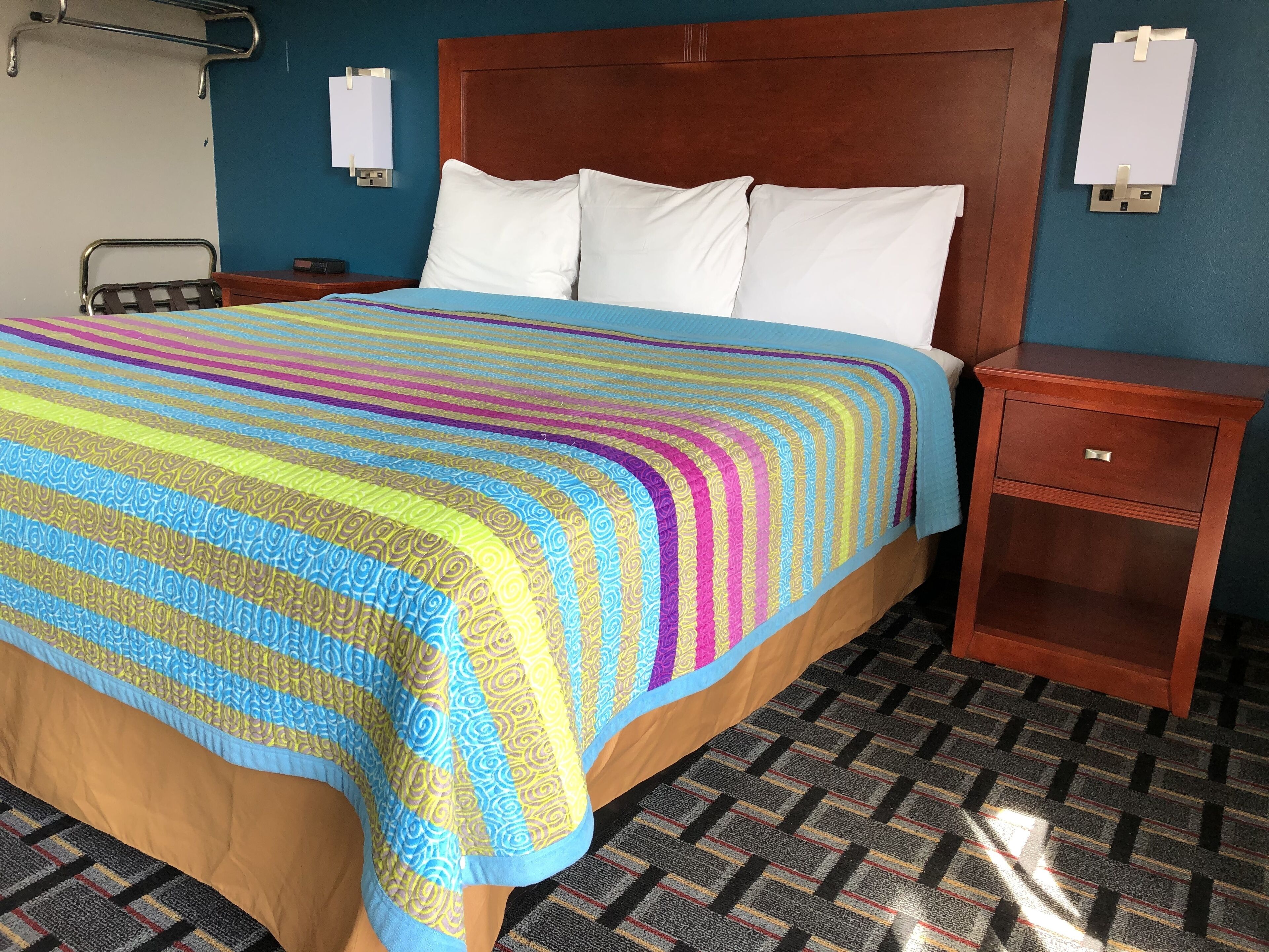 A hotel room with a large bed, a wooden headboard, a nightstand, and a wall-mounted light fixture.