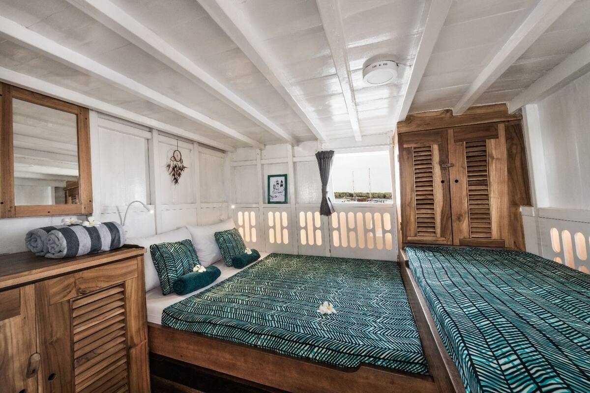 A cabin with two beds, a wooden dresser, a mirror, and a window with a view.