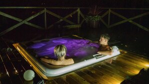 Un jacuzzi con dos personas, rodeado por una terraza de madera y una barandilla.