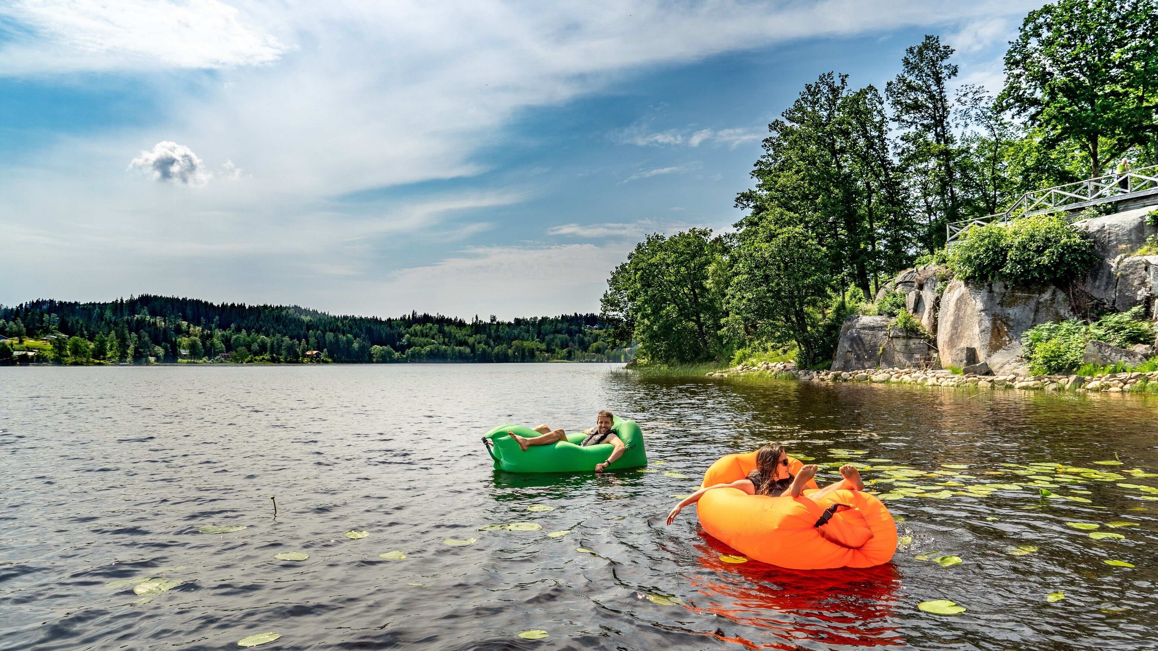 Duas pessoas flutuando em um lago calmo em boias infláveis.