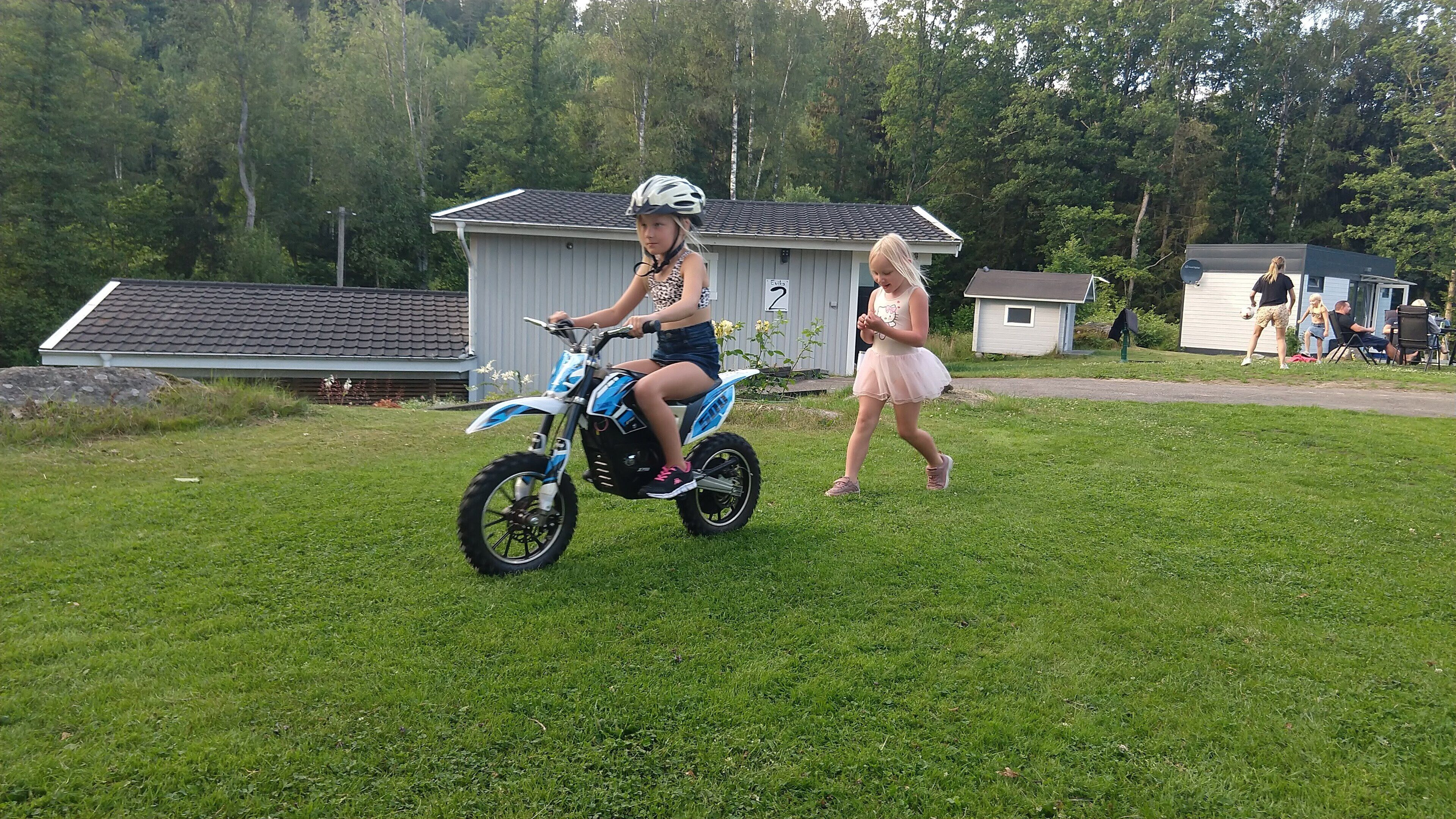 A grassy area with a small building and a person on a blue scooter.