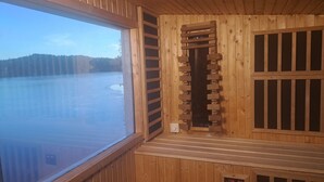 Una sauna de madera con un amplio ventanal que da a un paisaje nevado.